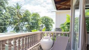 A balcony with a wicker chair, a large white vase, and a small table. - Romance Bungalows  (Mahé Island)