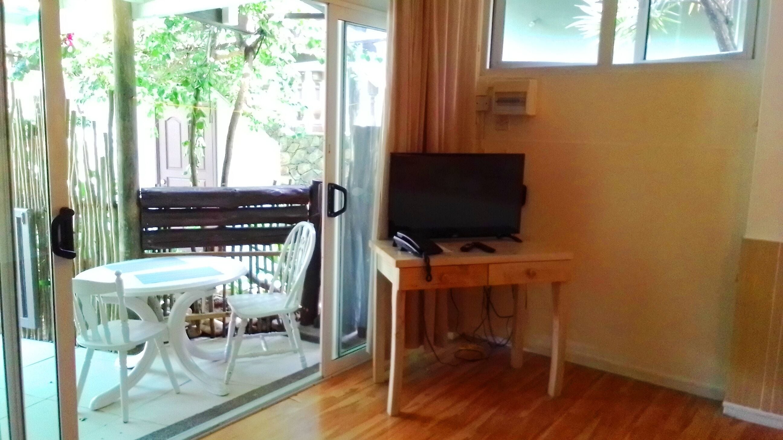 A room with a wooden floor, a TV on a wooden stand, a white table, and a white chair.