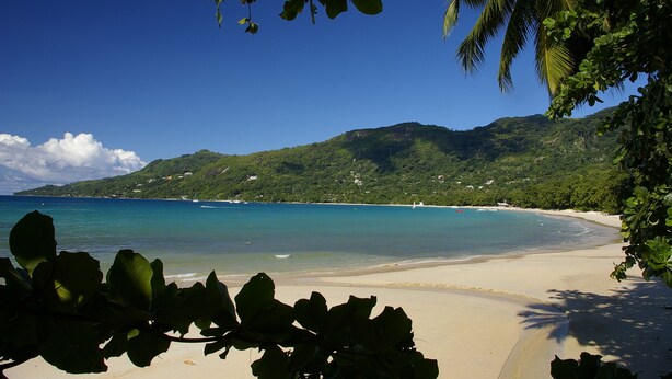A beach with clear turquoise water, a sandy shore, and lush green hills in the background. - Romance Bungalows  (Mahé Island)
