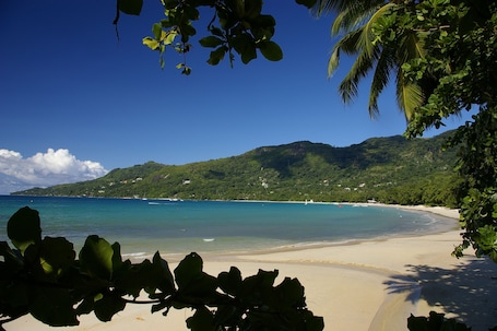 A beach with clear turquoise water, a sandy shore, and lush green hills in the background.
