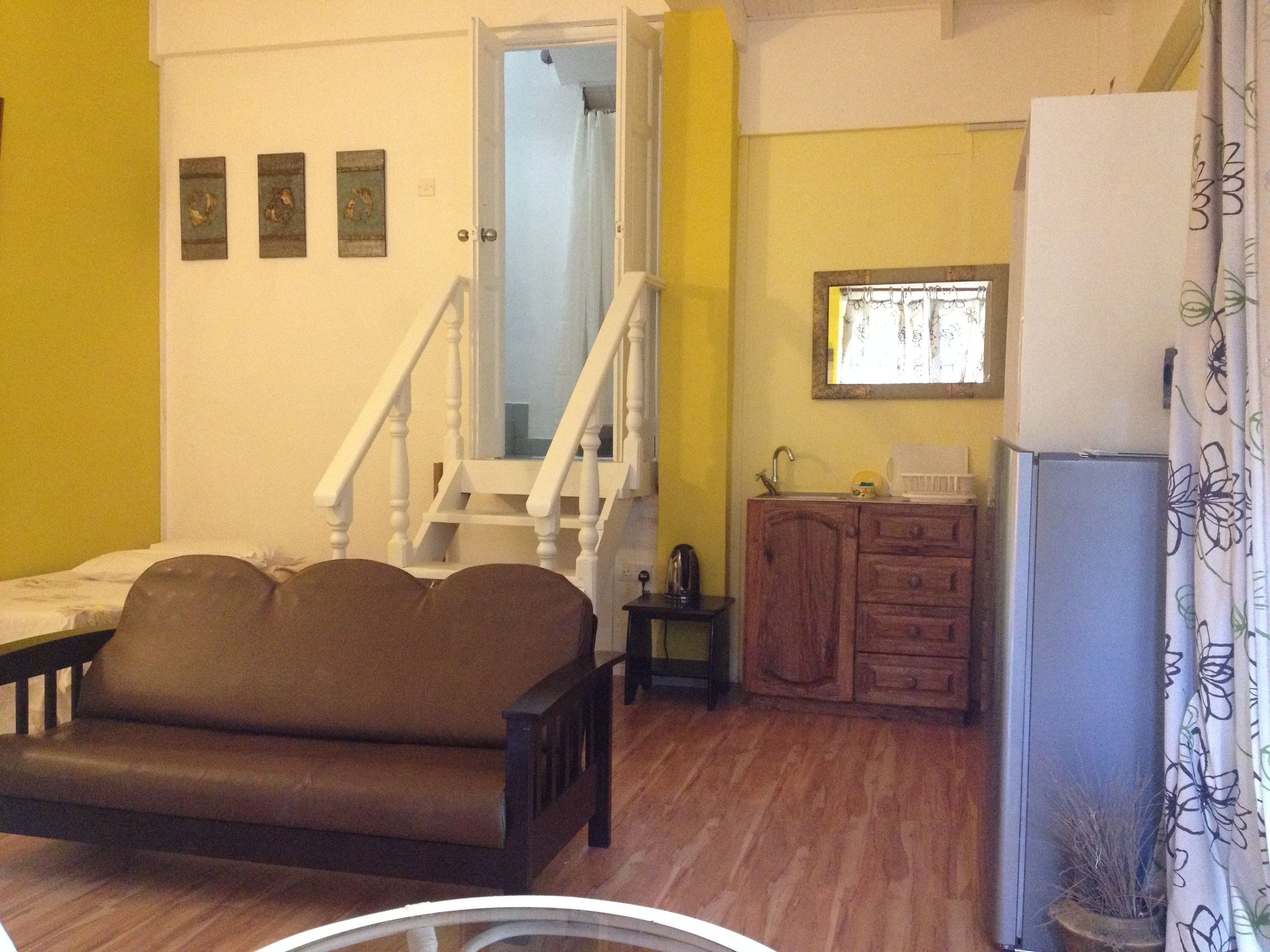Una sala de estar con un sofá marrón, un mueble de madera, un lavabo y una escalera que lleva a otra habitación.