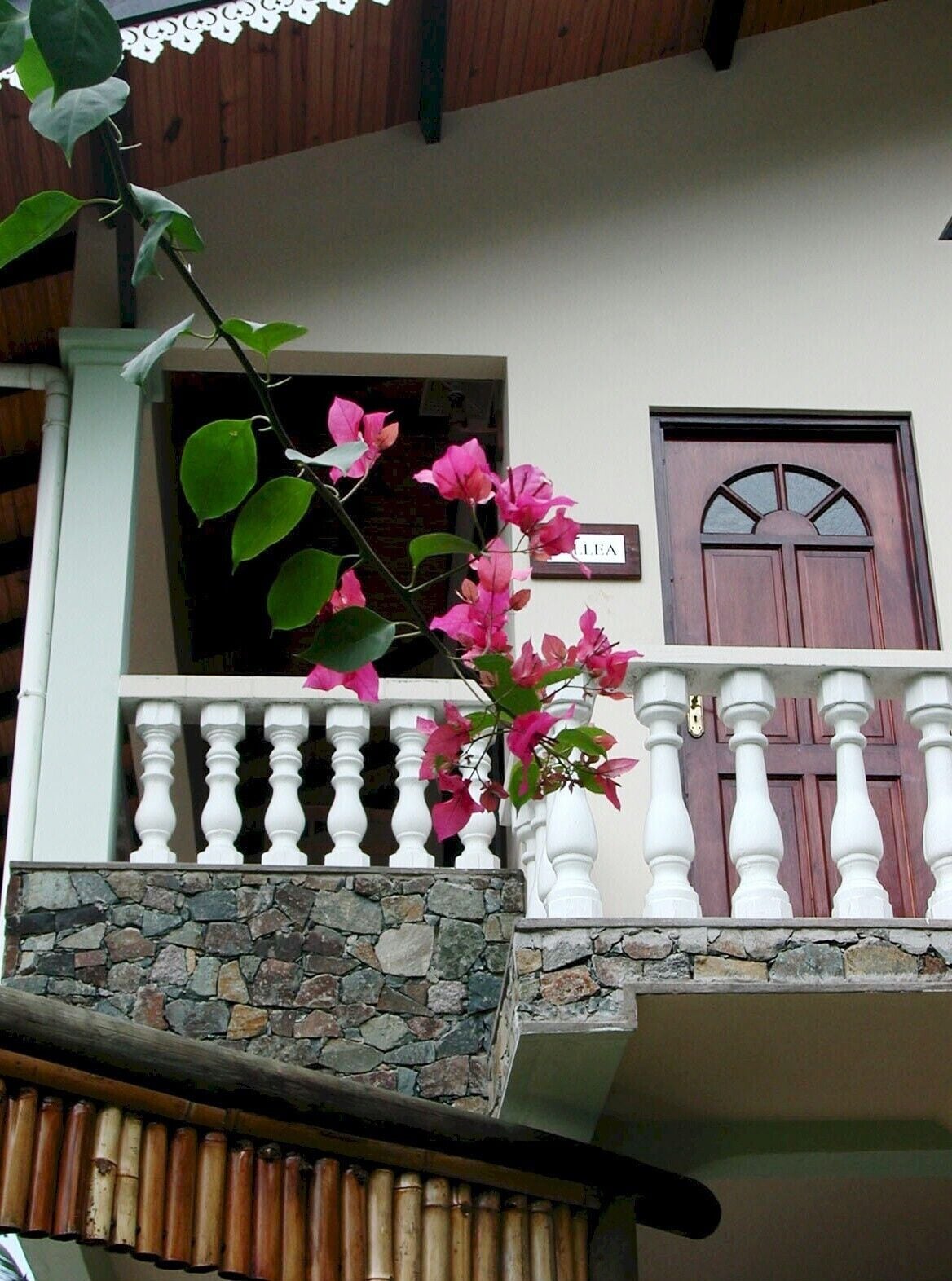 A building with a stone facade, a wooden balcony with white balustrades, and a wooden door with a glass panel.