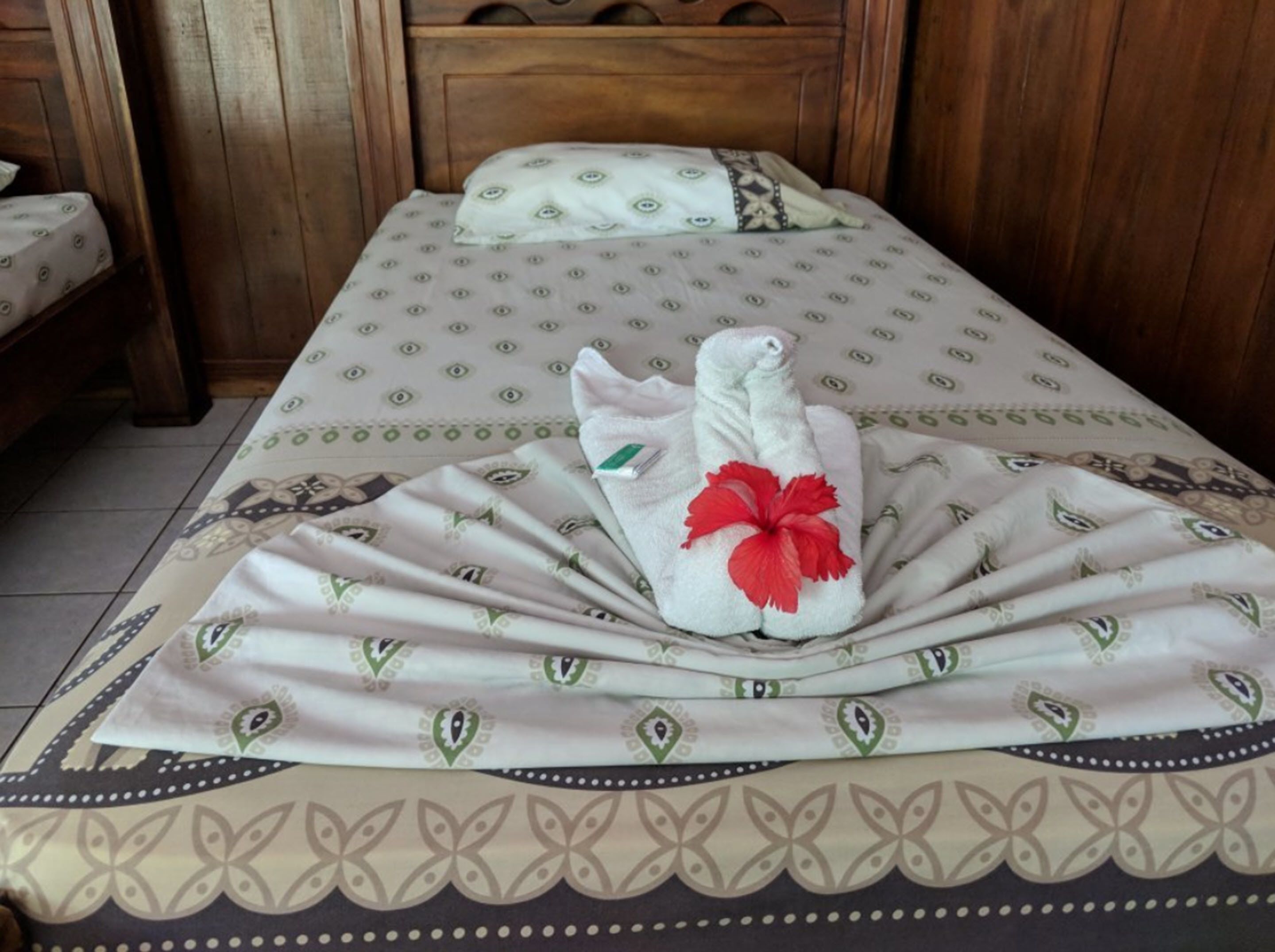Una cama bien hecha con una colcha estampada, un cojín con un diseño similar y una toalla con una flor roja.