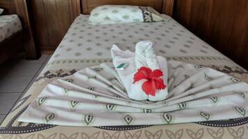 Una cama bien hecha con una colcha estampada, un cojín con un diseño similar y una toalla con una flor roja.
