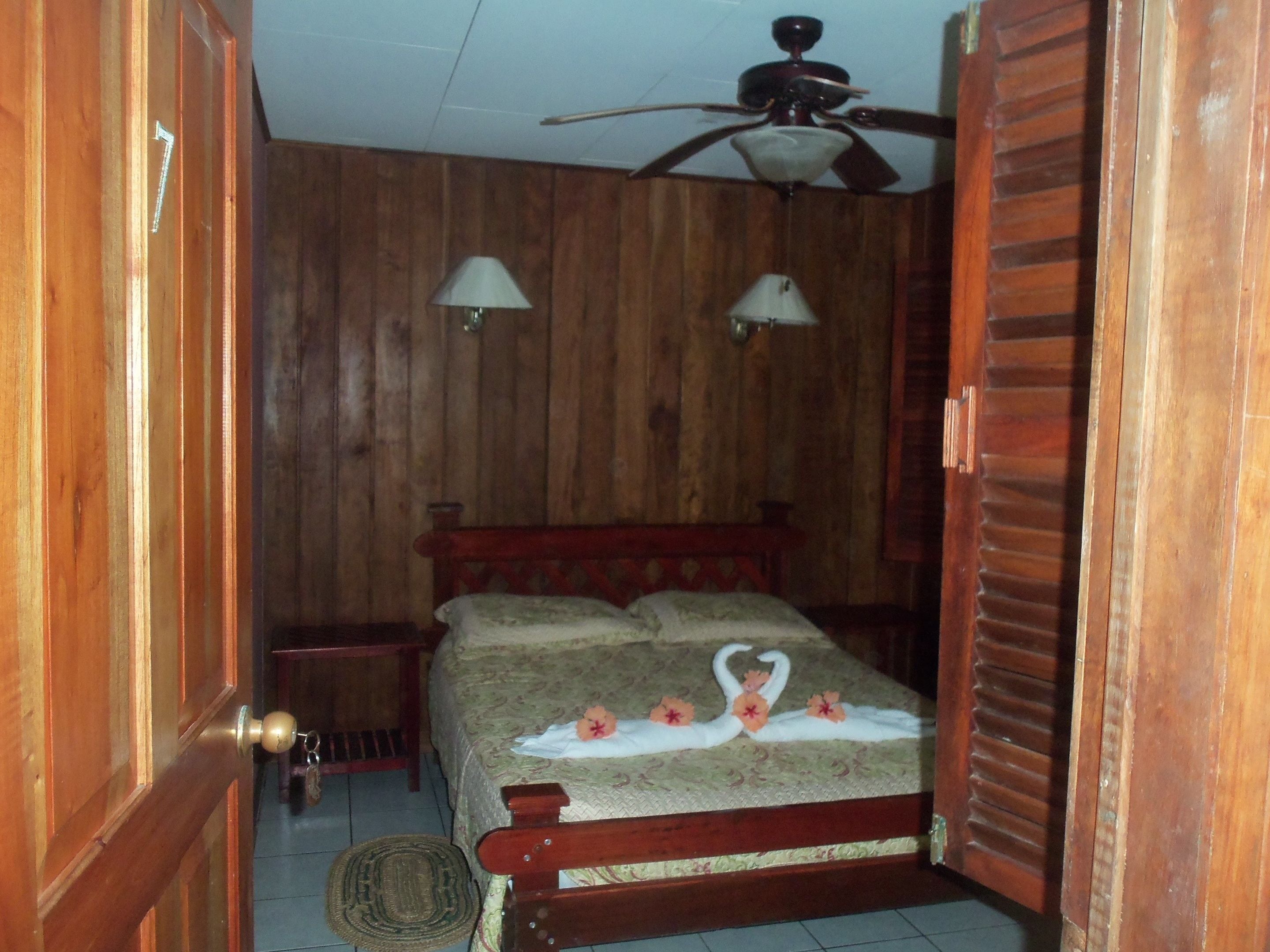 A wooden-paneled bedroom with a bed, two wall-mounted lamps, and a ceiling fan.