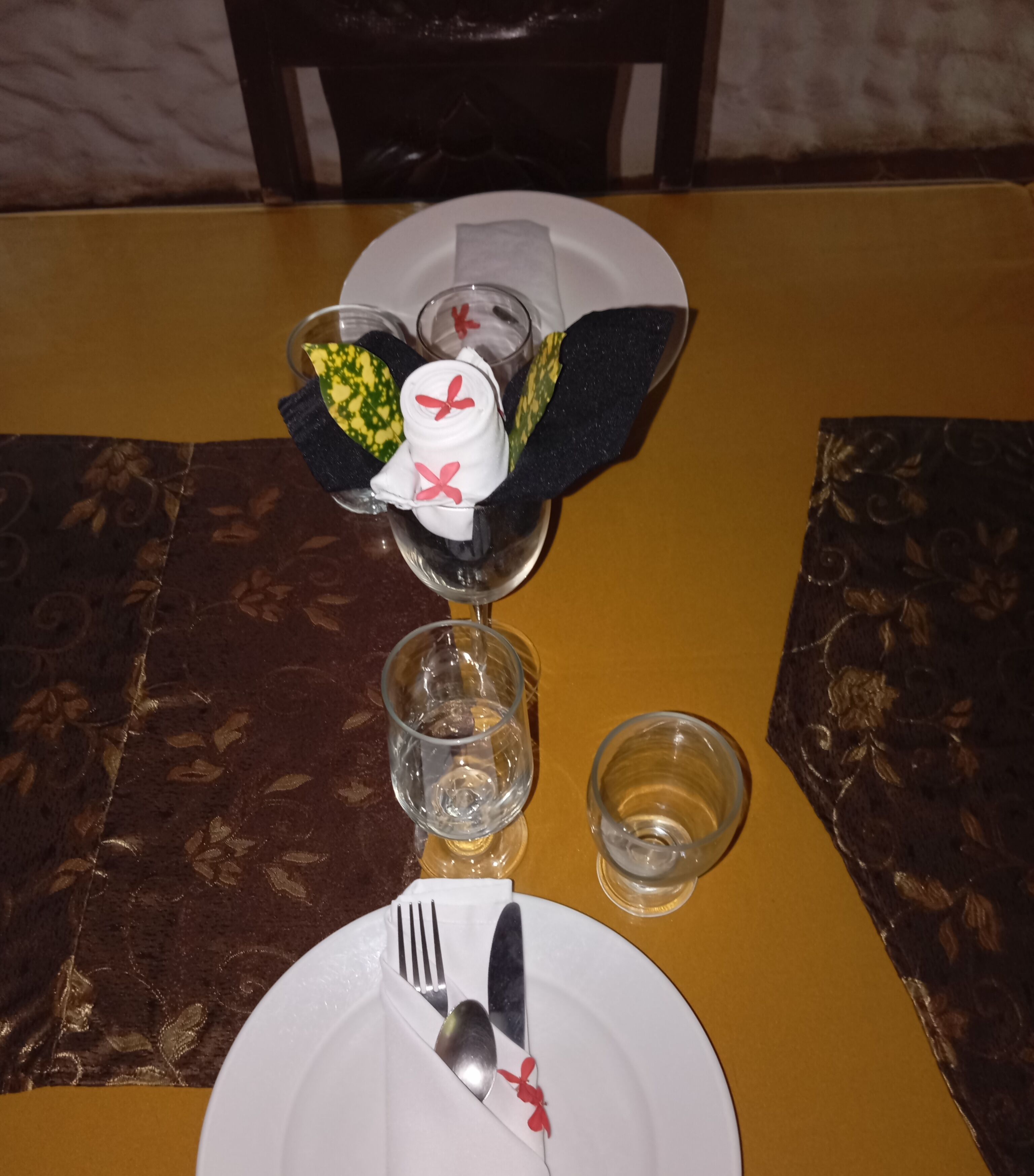 A table set with a white plate, a folded napkin, a glass with a decorative napkin, a fork, a knife, and a spoon.