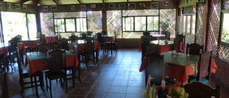 Un ristorante con tavoli e sedie in legno, coperto da un tetto con struttura a reticolo.