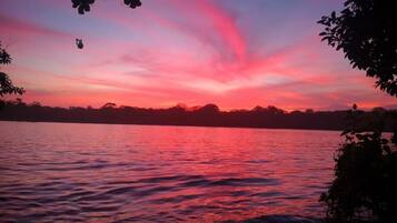 Un atardecer sobre un cuerpo de agua, con siluetas de árboles y un horizonte lejano.