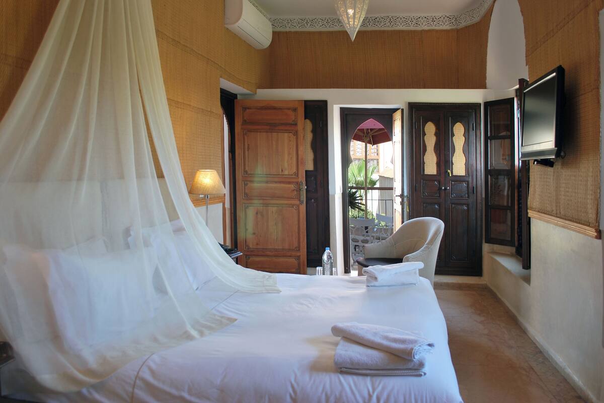 Una habitación con una cama, una silla, un televisor y una puerta que da al exterior.