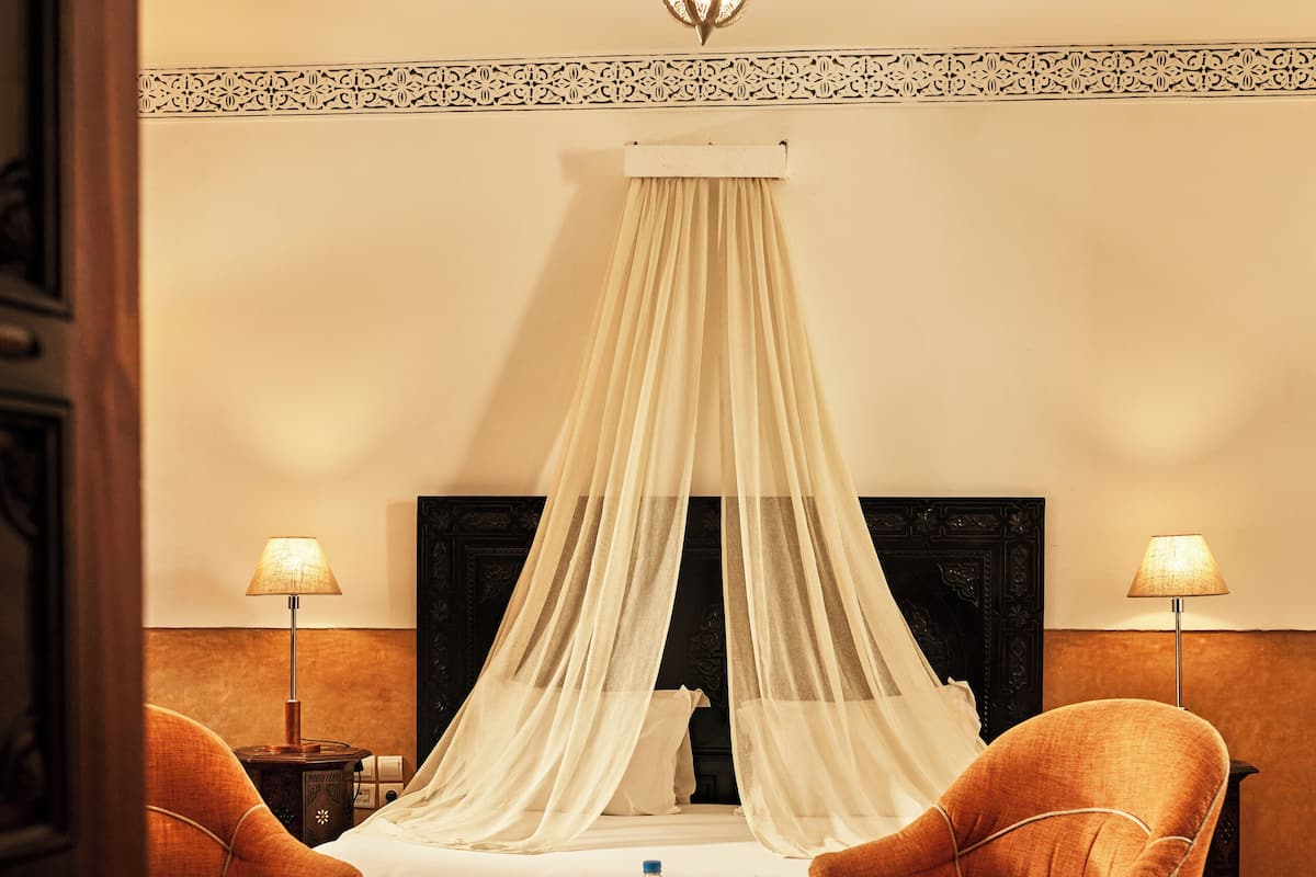 Una habitación con una cama con dosel, dos sillas, una mesita y una lámpara colgante.