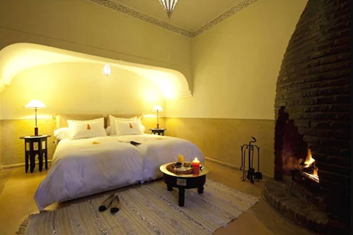 Un dormitorio acogedor con una cama grande, dos lámparas de noche, una mesita con velas y una chimenea.