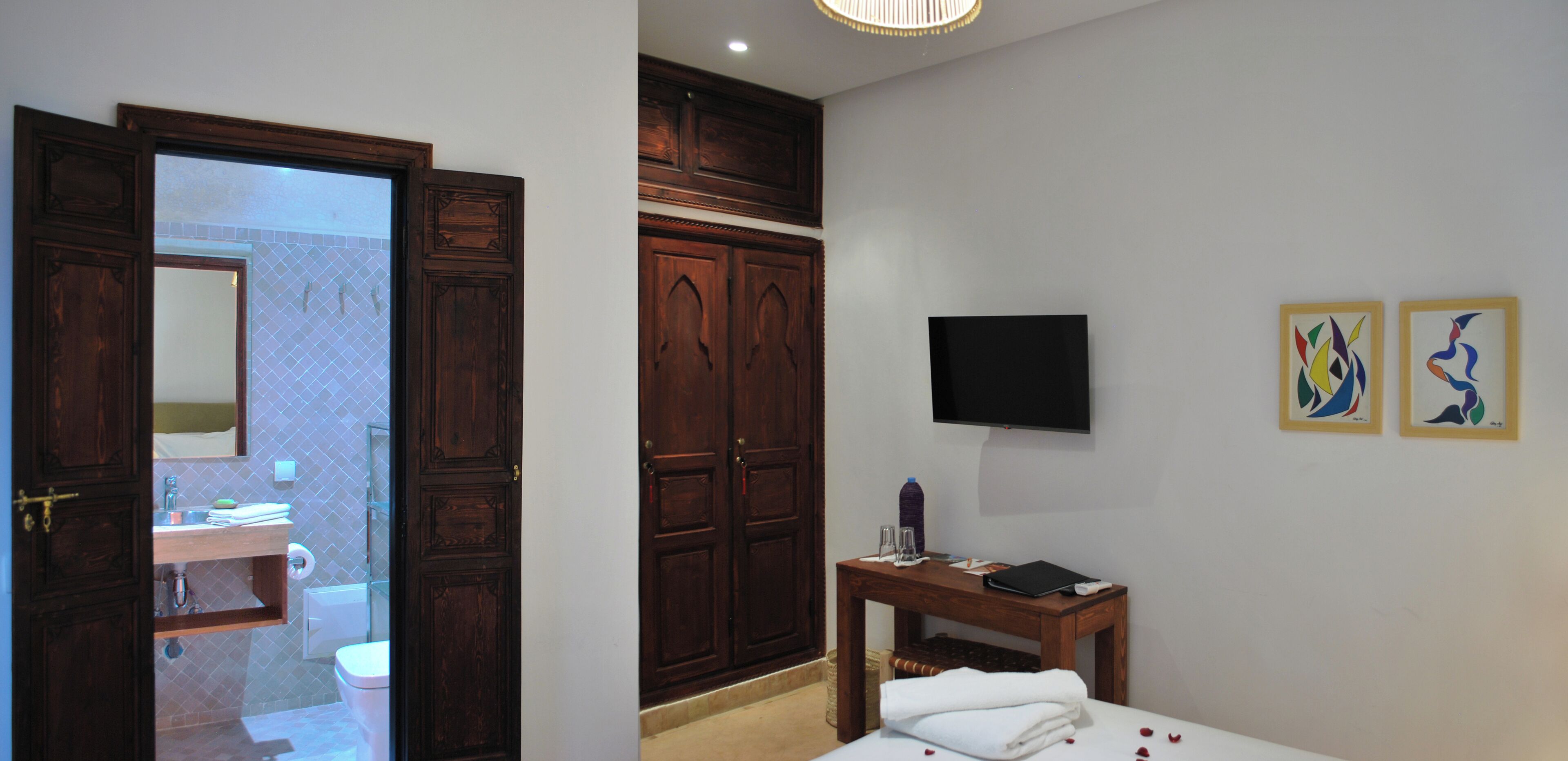 A hotel room with a wooden wardrobe, a television, and two abstract paintings on the wall.