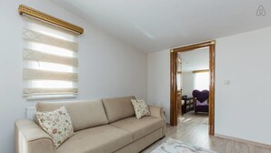 A living room with a beige sofa, patterned cushions, a decorative window blind, and a colorful rug. - Taximum Suites (Istanbul)