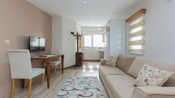 A modern living room with a sofa, a TV, and a dining area with a table and chairs. - Taximum Suites (Istanbul)
