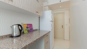 A kitchen with a granite countertop, a kettle, a refrigerator, and a door leading to another room. - Taximum Suites (Istanbul)