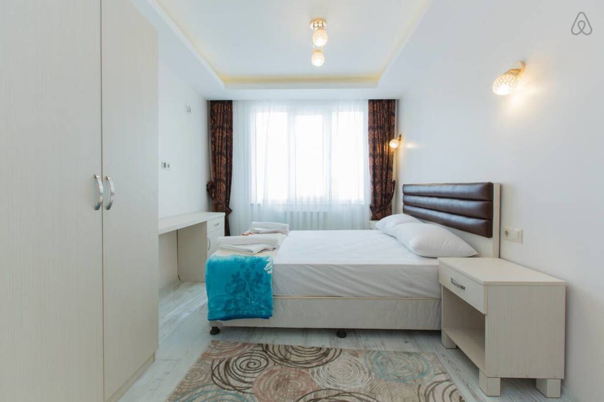 A bedroom with a bed, bedside table, wardrobe, and a window with curtains.