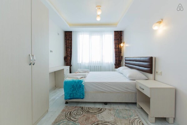 A bedroom with a bed, bedside table, wardrobe, and a window with curtains.