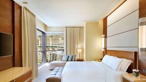 A hotel room with a large bed, a seating area, a TV, and a view of a cityscape.