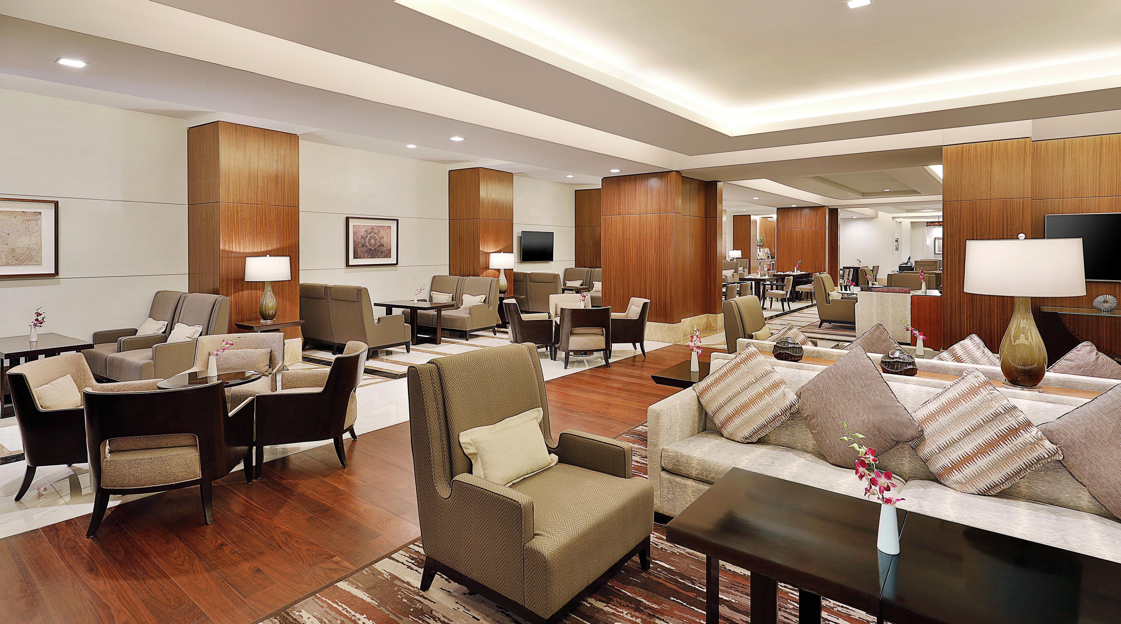 A spacious hotel lobby with multiple seating areas, a flat-screen TV, and a reception desk.