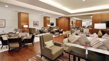 A spacious hotel lobby with multiple seating areas, a flat-screen TV, and a reception desk.