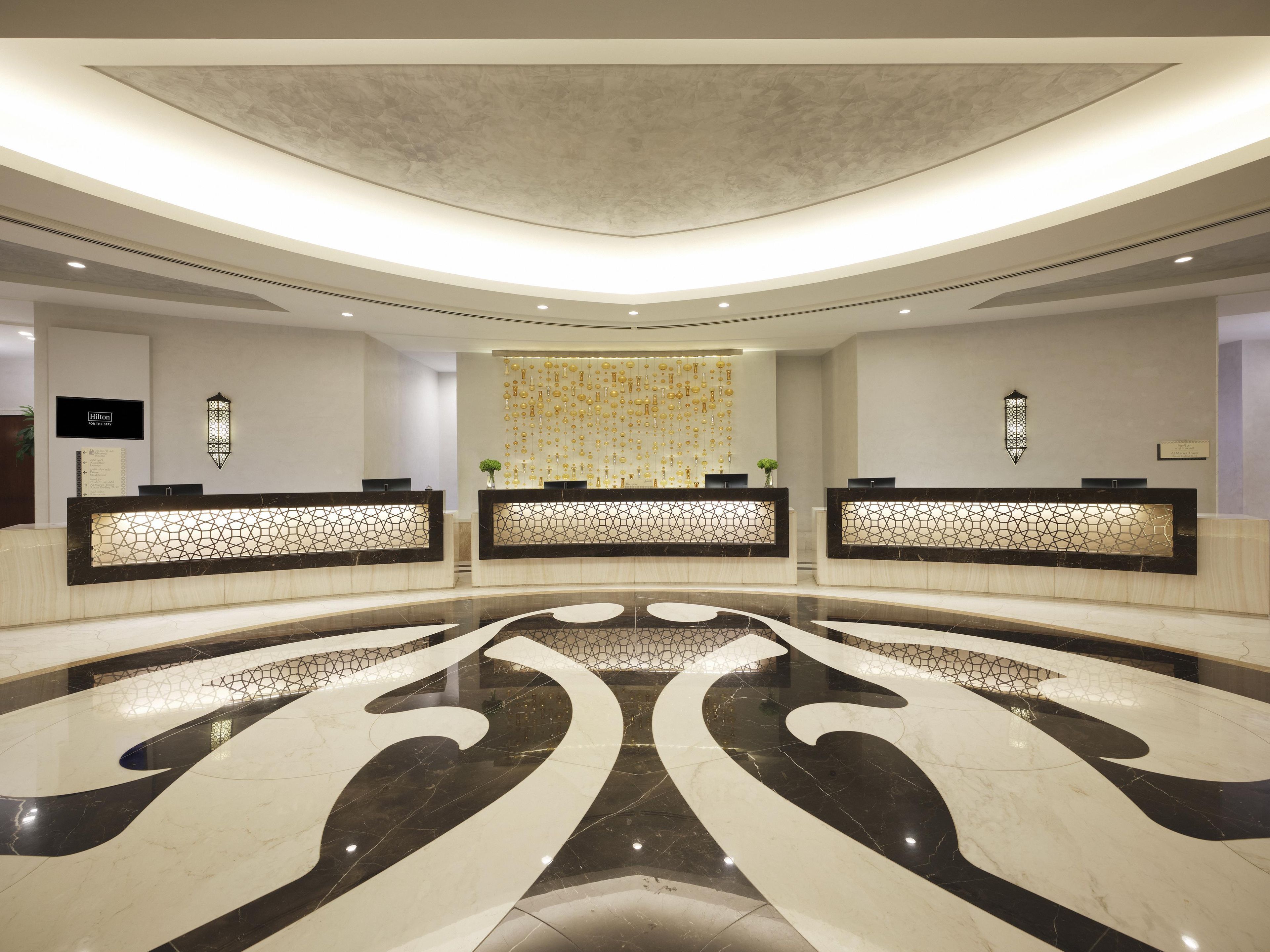 A hotel reception area with three counters, a decorative wall, and a large marble floor design.