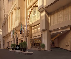 A hotel entrance with a grand facade, multiple flags, and a well-lit interior.