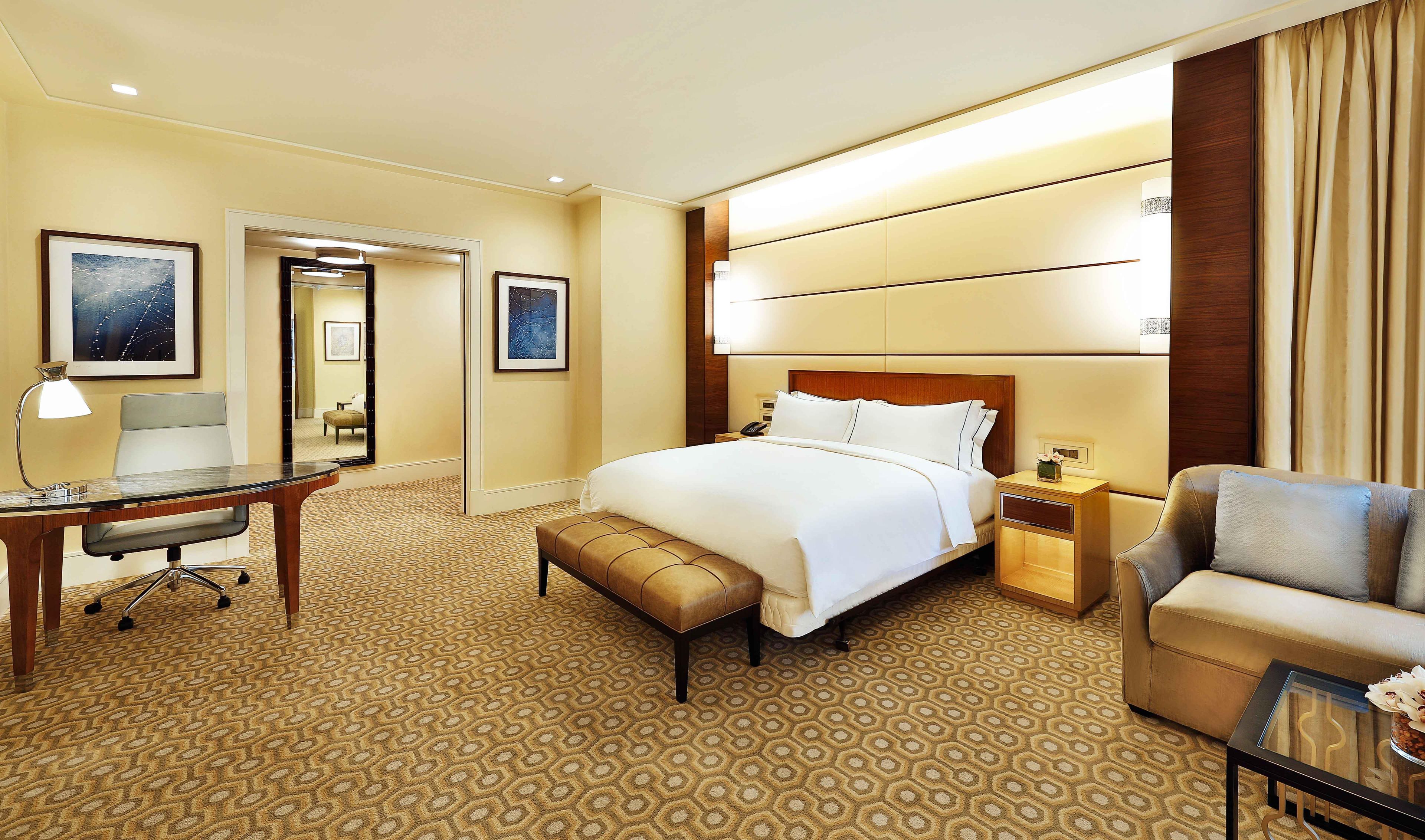 A hotel room with a large bed, a desk, a chair, a nightstand, and a sofa.