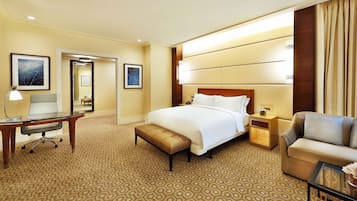 A hotel room with a large bed, a desk, a chair, a nightstand, and a sofa.