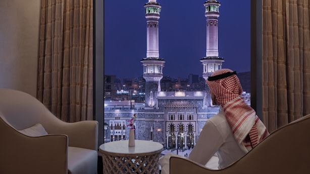 A view of a mosque with two minarets, a modern interior with a sofa and a small table, and a person in traditional attire.