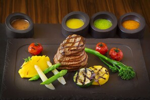 A meal with grilled steak, grilled vegetables, and four small bowls of sauces on a slate board.