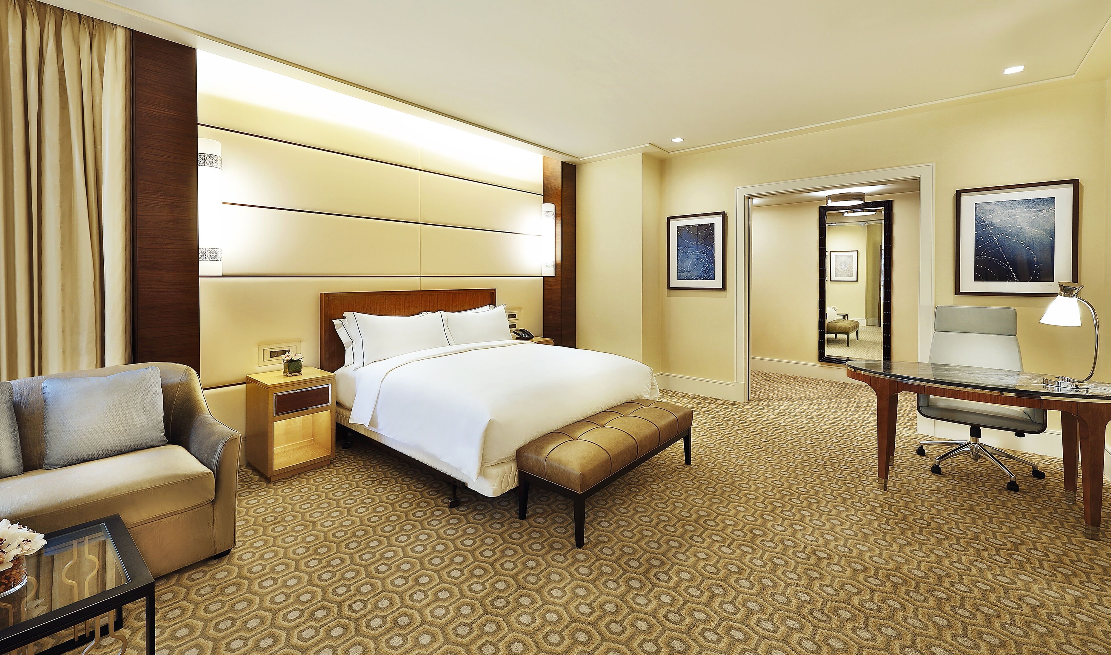 A hotel room with a large bed, a desk, a chair, a nightstand, and a mirror.