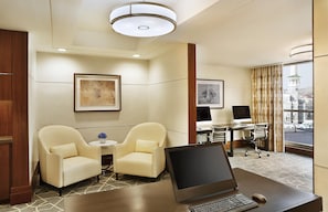 A hotel room with a desk, two armchairs, a small table with a vase, and a large window with a view of a tower. - Conrad Jabal Omar Makkah (Makkah)