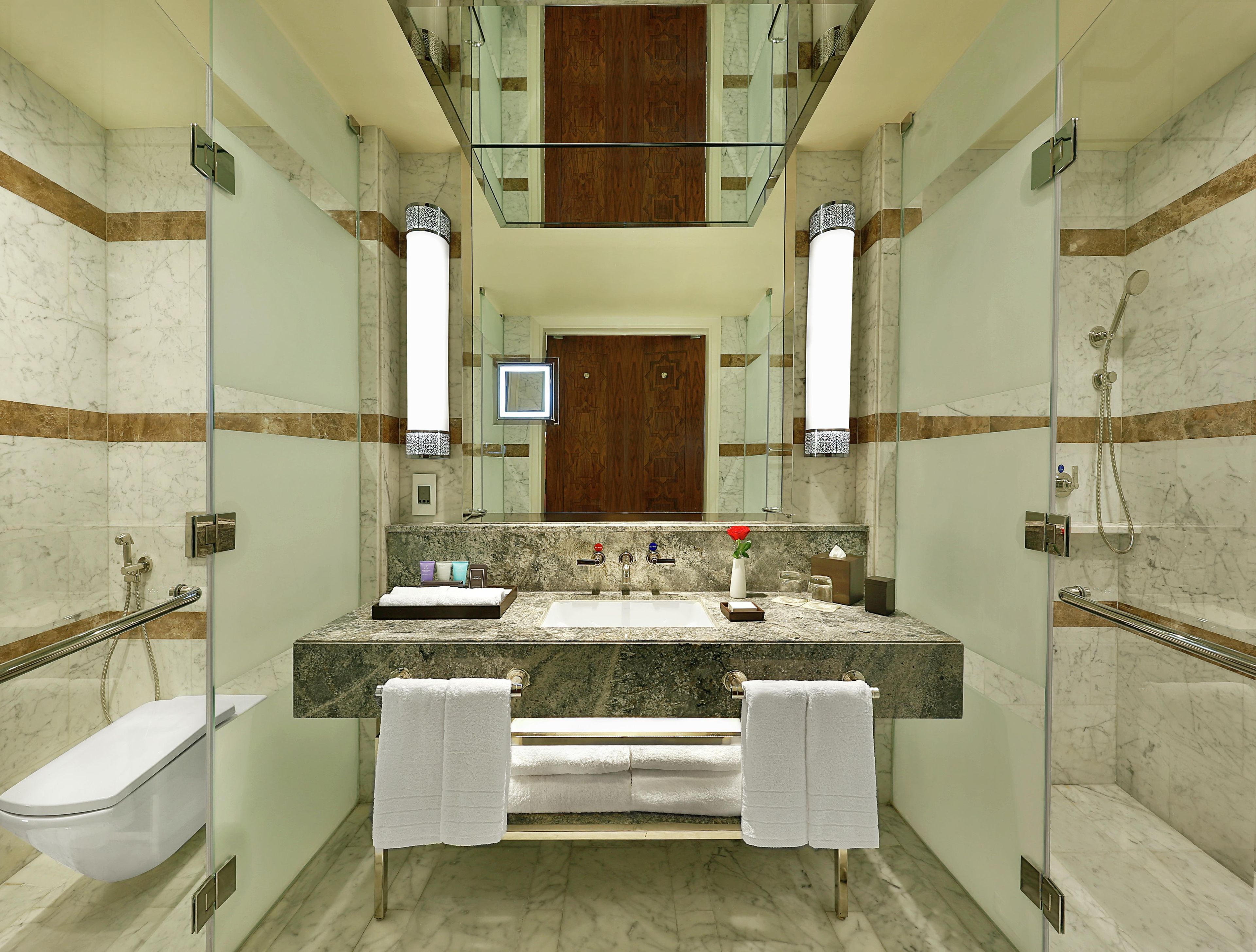 Un baño moderno con cabina de ducha de vidrio, lavamanos de mármol y puerta de madera.