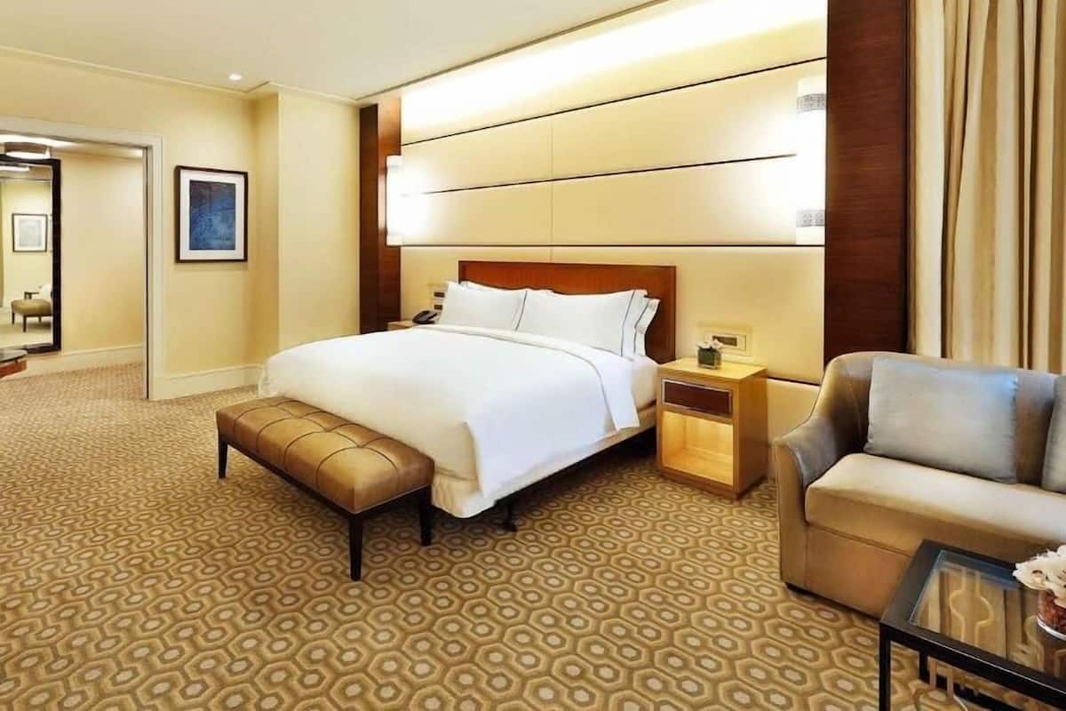 A hotel room with a large bed, a bedside table, a chair, and a patterned carpet.