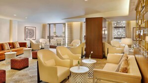 A spacious hotel lobby with a large seating area, a view of a mosque, and a decorative wall with geometric patterns.