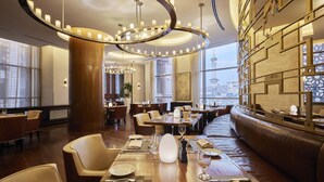 A modern restaurant with a central seating area, high ceilings, and a view of a tower through large windows.