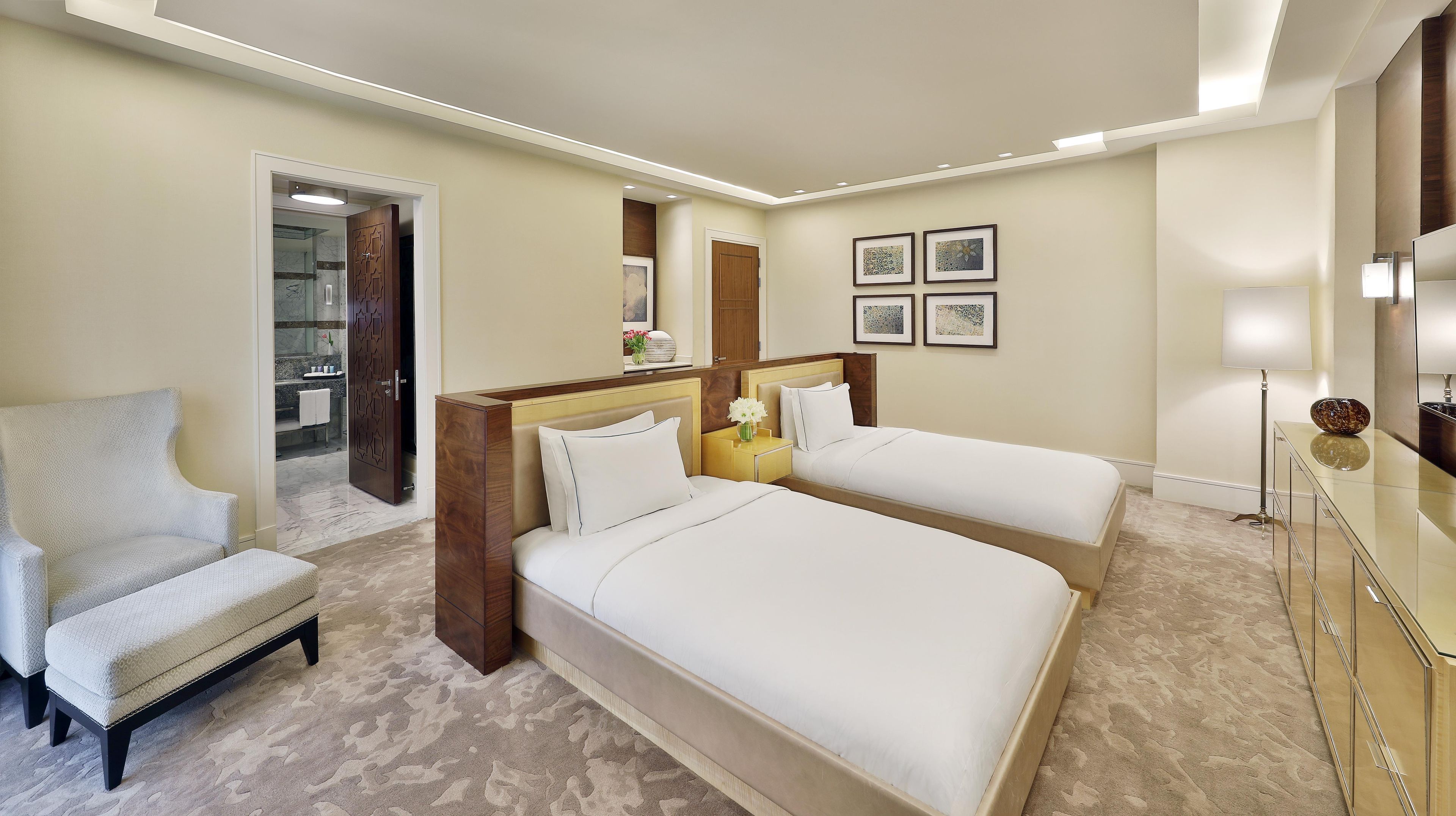 A hotel room with two beds, a sitting area, a bathroom, and a mirror.