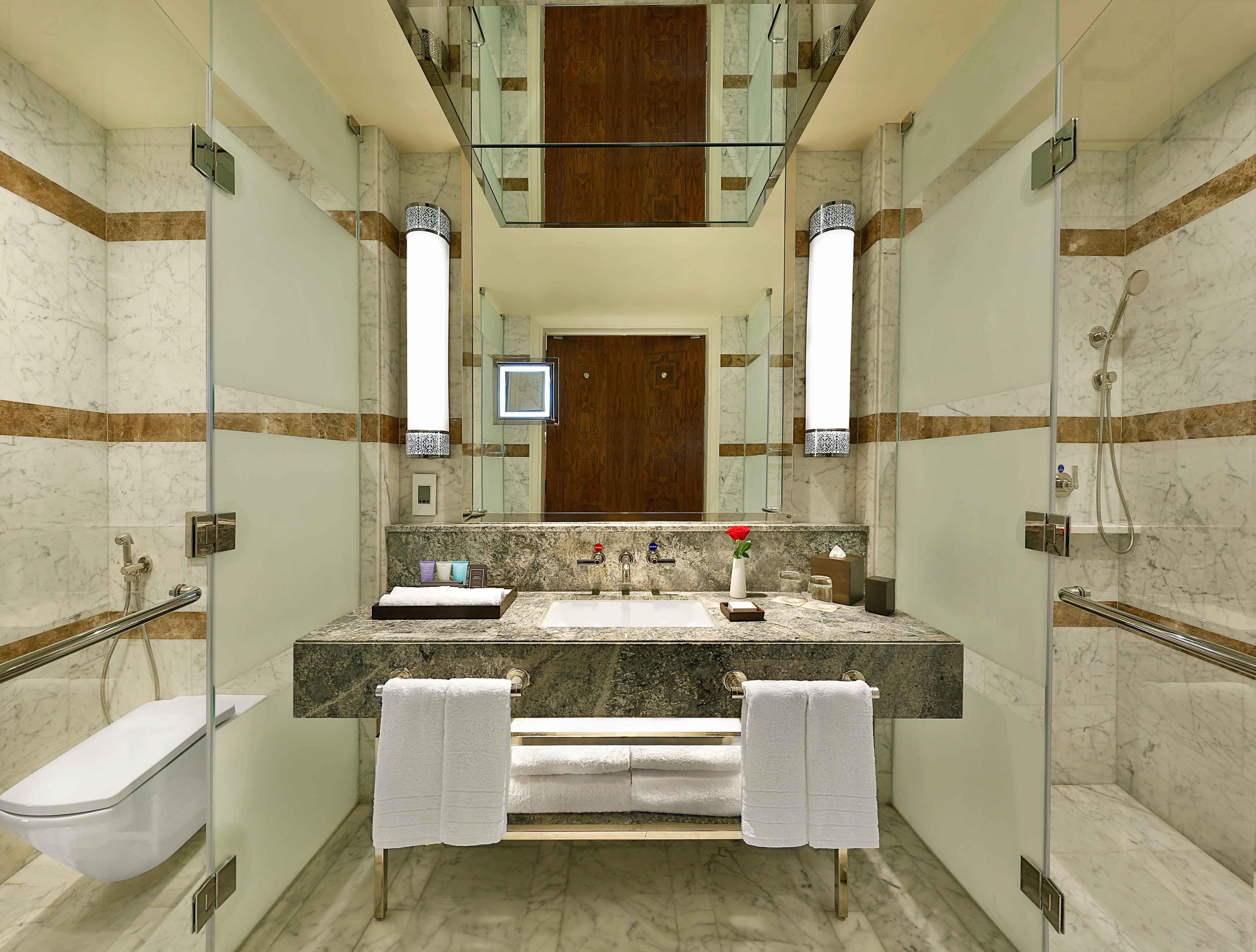 A modern bathroom with a glass-enclosed shower, a marble sink, and a wooden door.