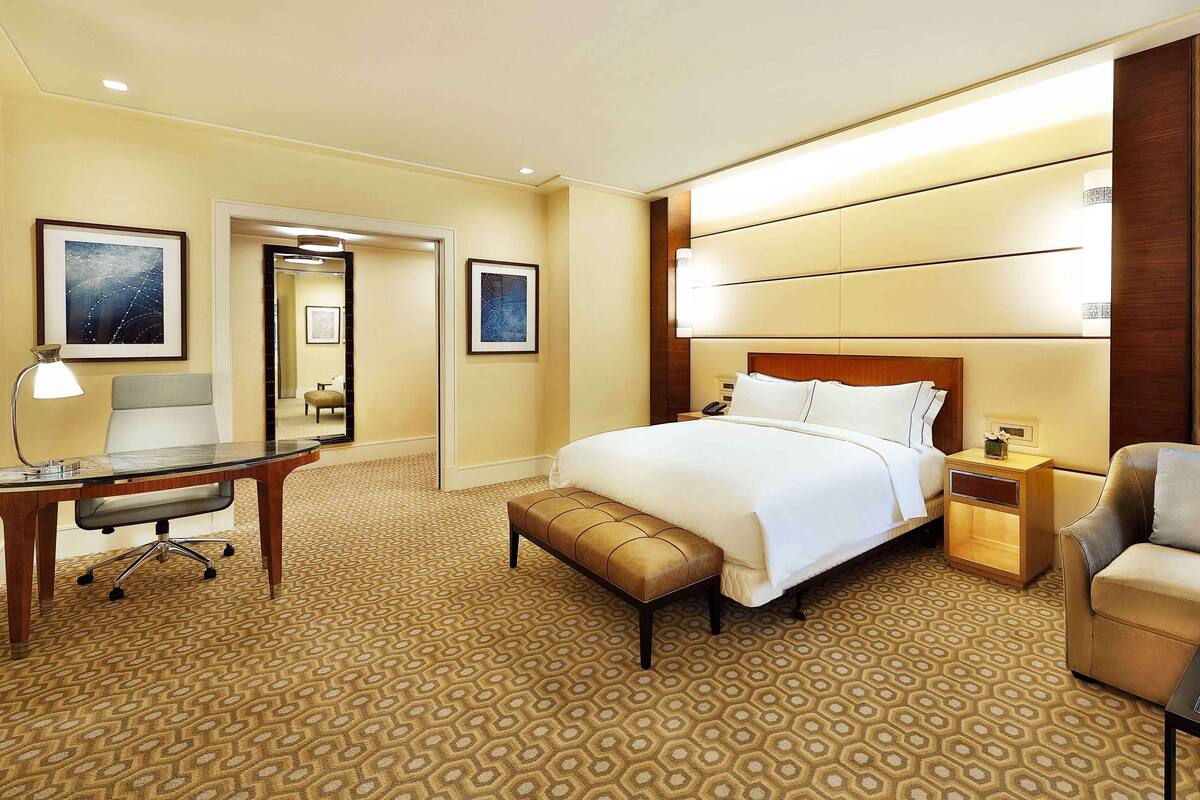 A hotel room with a large bed, a desk with a lamp, a chair, a nightstand, and a sofa.