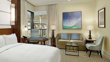Habitación de hotel con cama, sofá, sillón, una pequeña mesa y vista a la ciudad a través del ventanal.