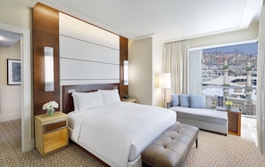 Habitación de hotel con una cama grande, un sofá, una mesita de noche y vistas a un paisaje urbano.