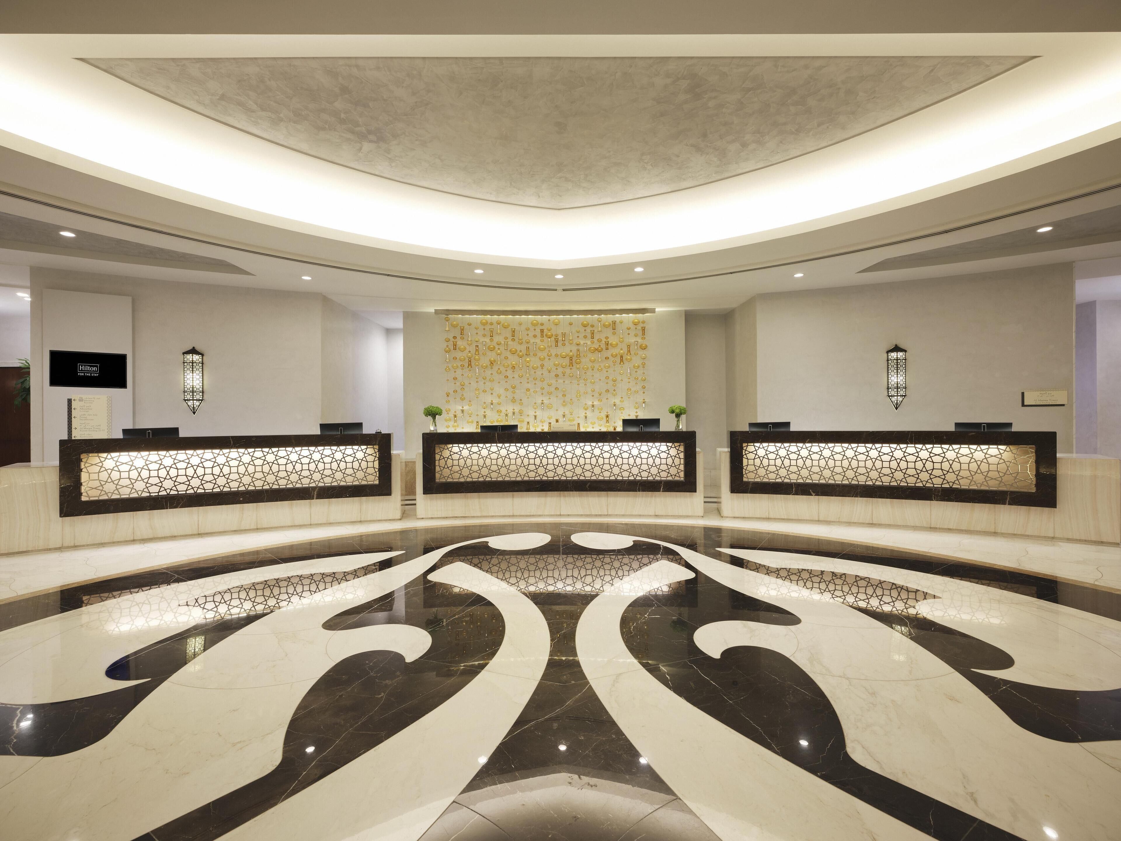 A hotel reception area with three reception desks, a decorative wall, and a large, reflective floor design.