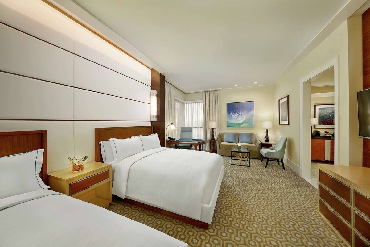 A hotel room with two beds, a desk, a chair, a TV, and a painting on the wall.