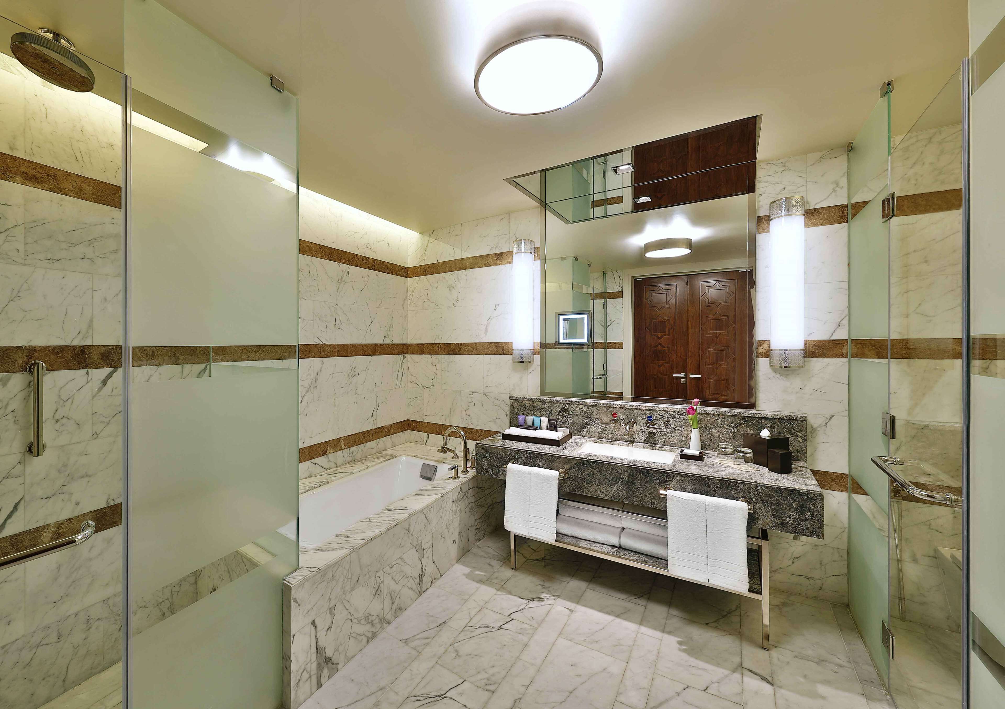 A modern bathroom with a glass-enclosed shower, a marble-tiled floor, a built-in sink, and a large mirror above the vanity.