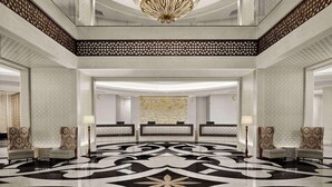 A spacious lobby with a geometric patterned floor, a large ornate chandelier, and a reception desk.