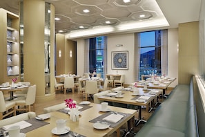 Un comedor de hotel moderno con varias mesas, sillas y una larga banca.