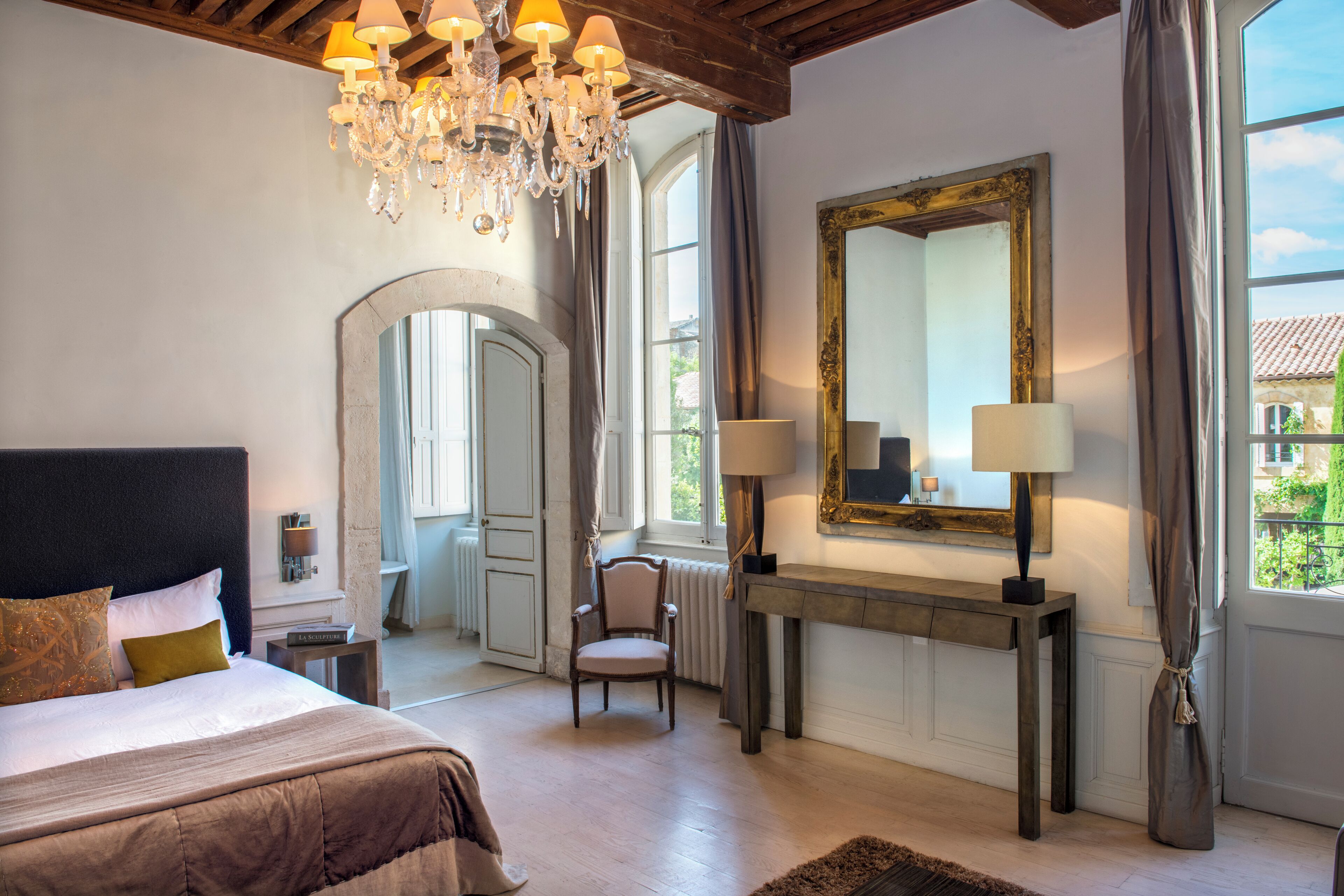 Een slaapkamer met een groot bed, een kroonluchter, een spiegel en een console met lampen.