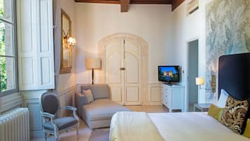 A bedroom with a bed, a sofa, a chair, a TV, and a large arched door.