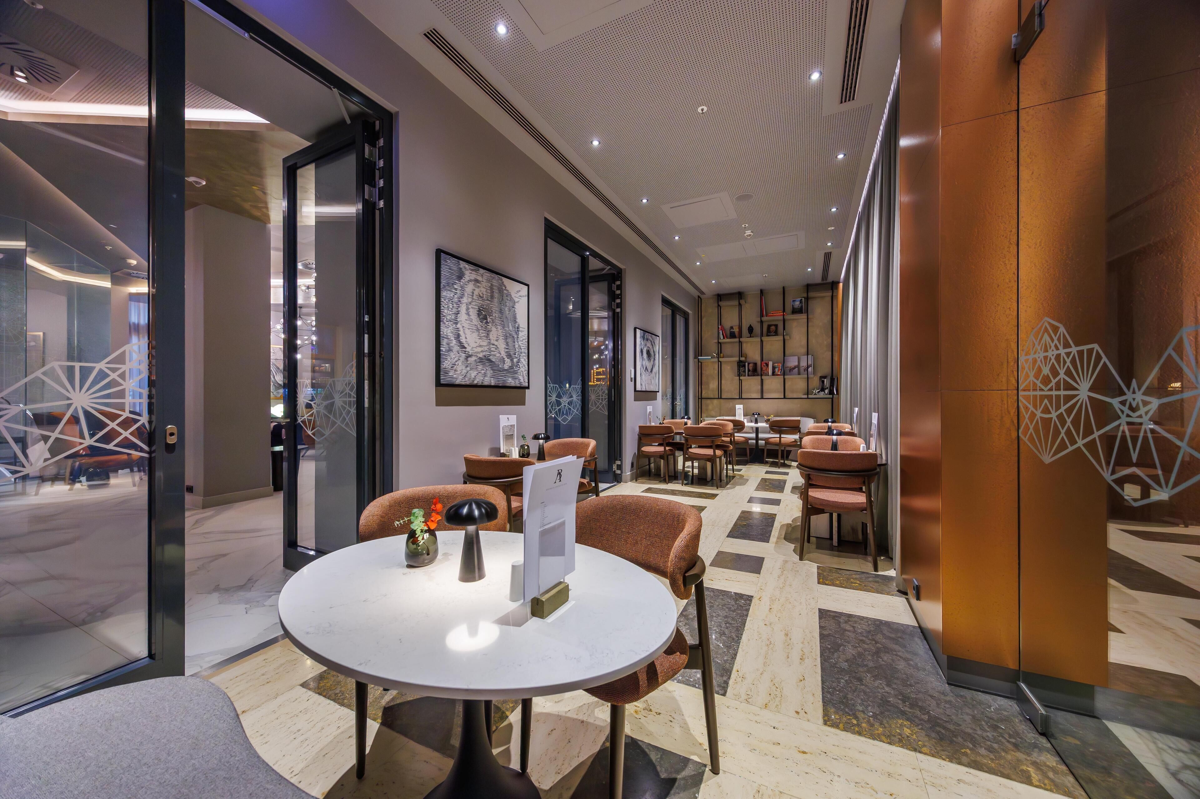 Un hall d’hôtel moderne avec une table ronde, un espace salon et une vue sur la rue.