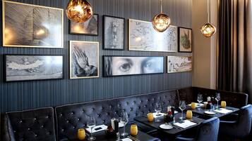 A restaurant with a dark, tufted booth seating area and multiple dining tables set with wine glasses, plates, and cutlery.